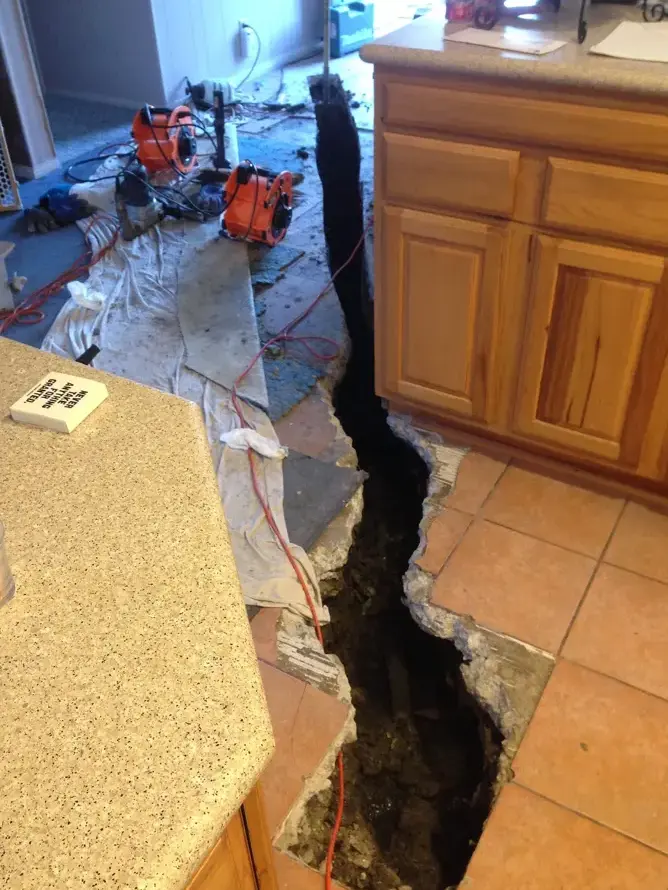 Trench cut through a kitchen tile floor to reach a slab leak