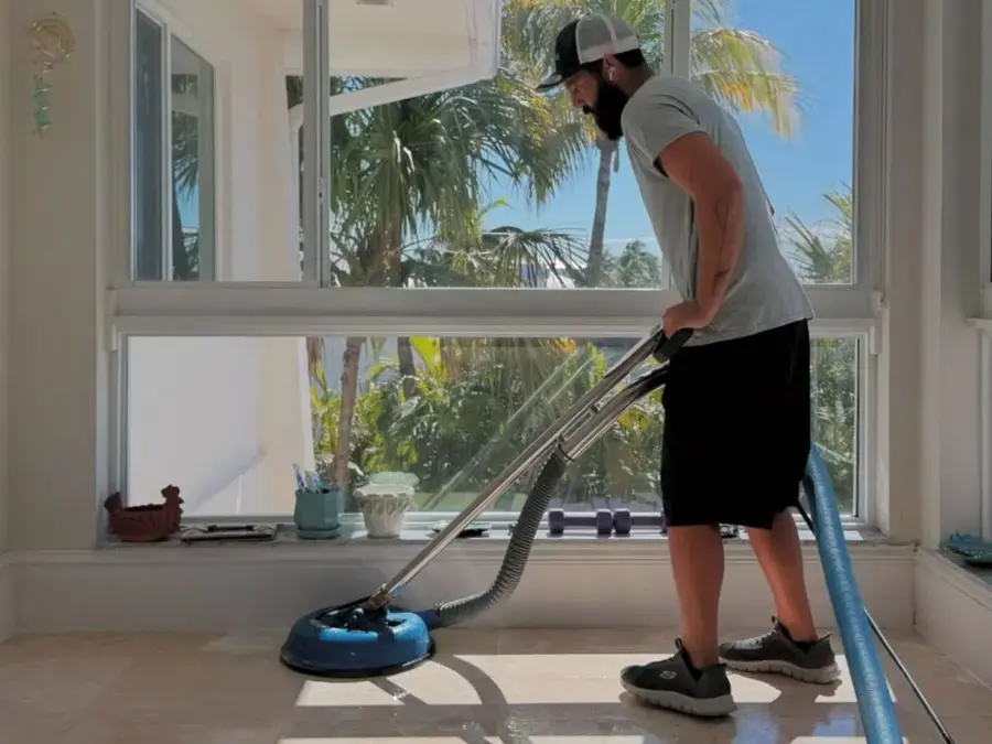 Technician extracting water from a tile floor in a Florida home with palms outside the window